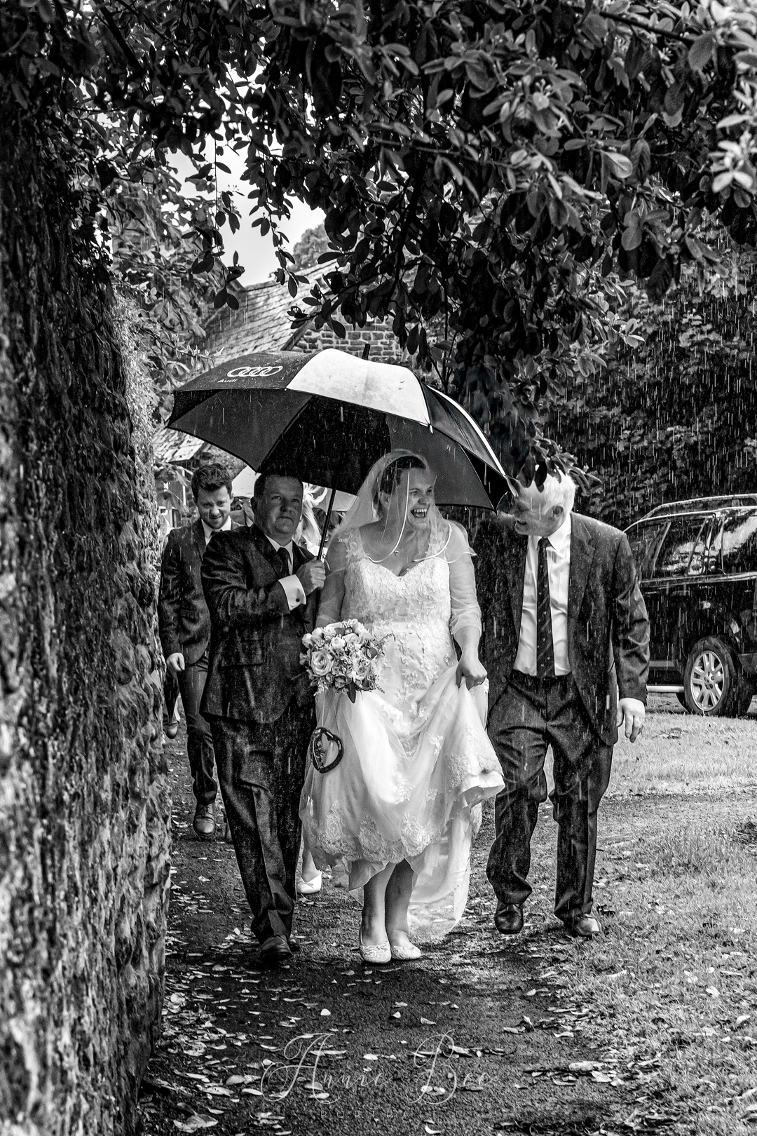Bride with husband and father walking in the rain under an umberella